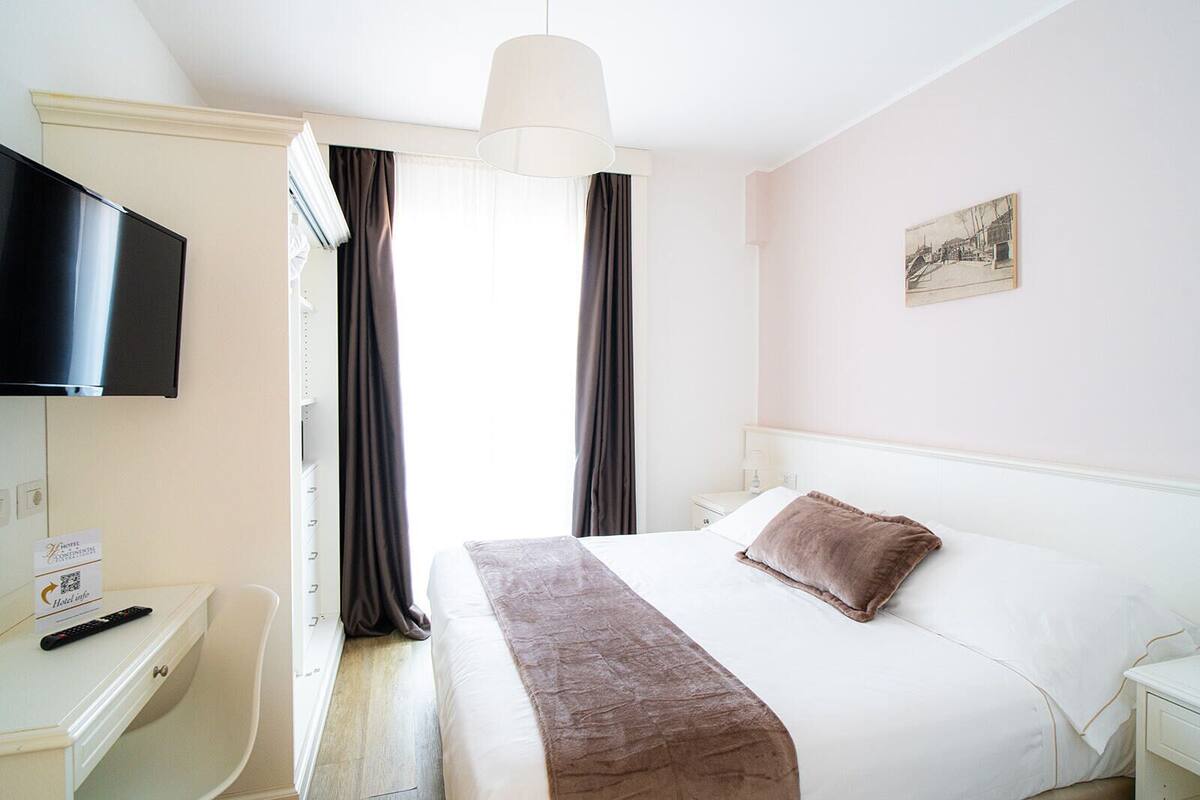 A hotel room with a bed, a television, a desk with a remote control, and a window with curtains.