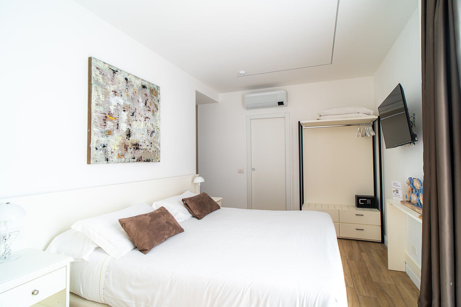 A bedroom with a bed, a bedside table, a TV, a wardrobe, and a painting on the wall.