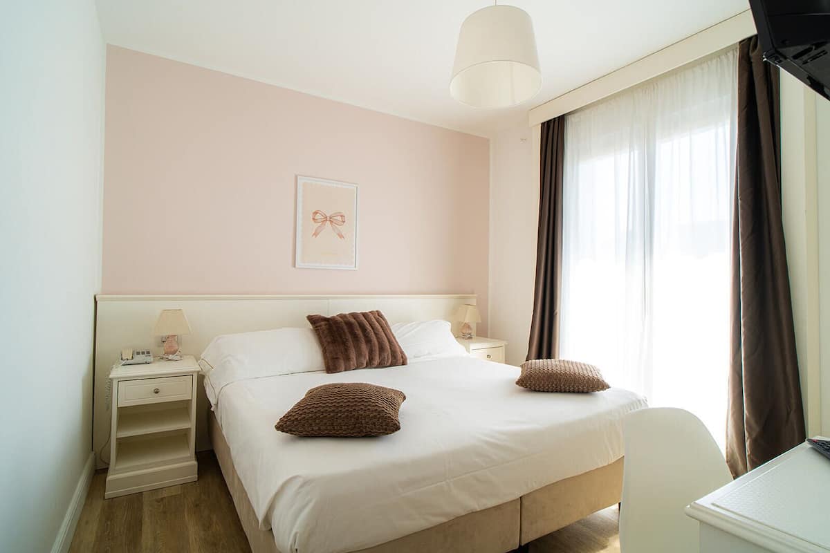 A neatly arranged bedroom with a bed, bedside tables, a desk, and a window with curtains.