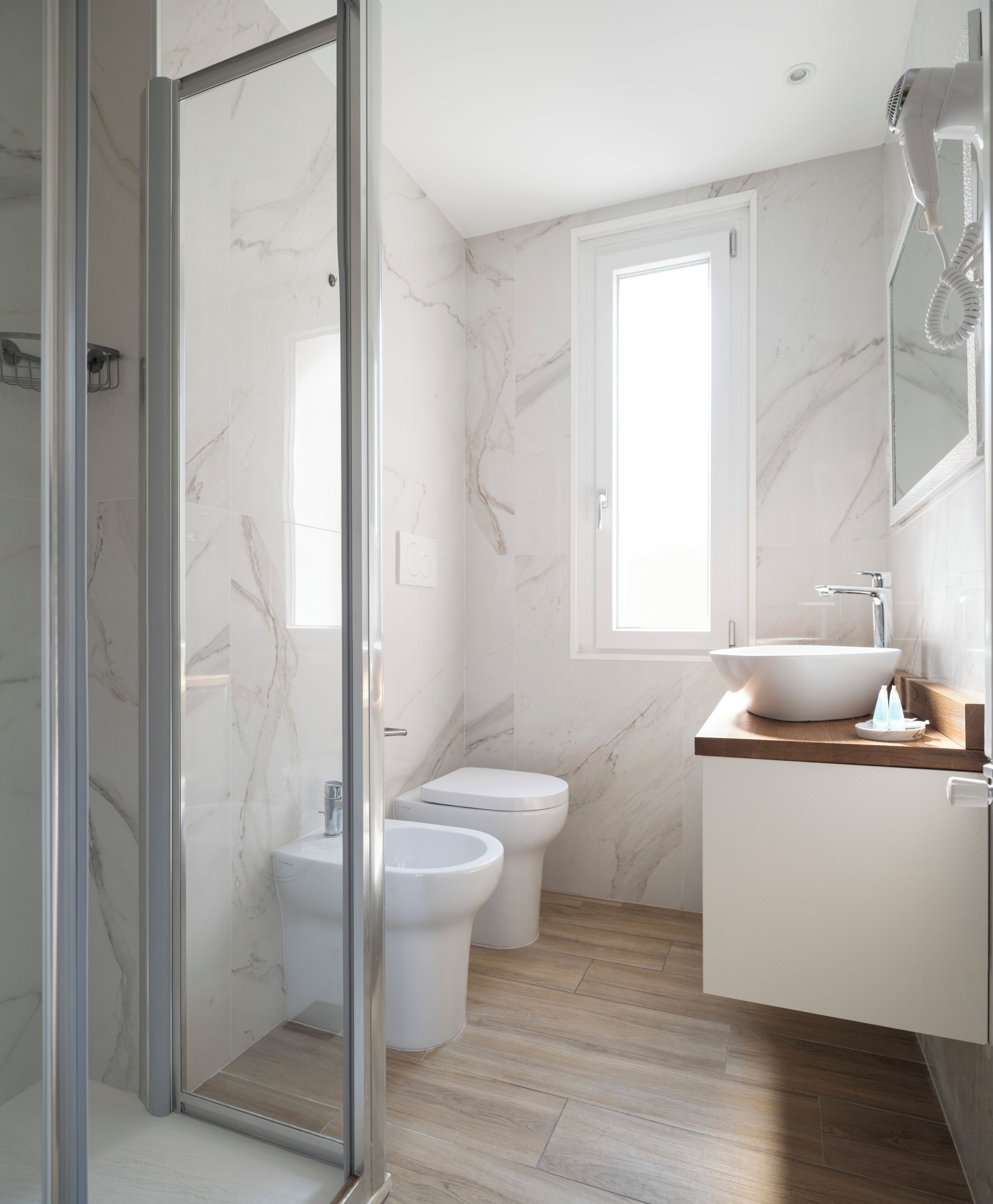 Un baño con cabina de ducha de vidrio, inodoro, bidé, lavabo y ventana.