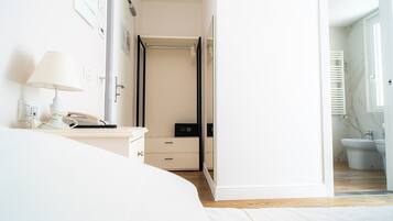Habitación de hotel con cama, mesita de noche con lámpara, teléfono, armario y baño visible a través de una puerta abierta.
