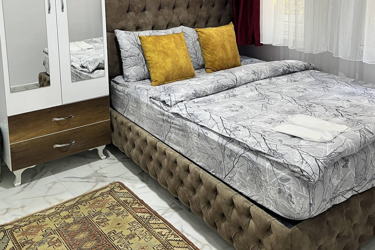 A bedroom with a bed, a wardrobe, an air conditioner, and a window with curtains.