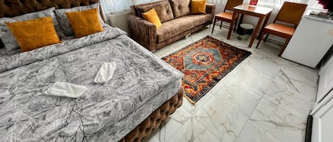A hotel room with a bed, a sofa, a dining table, and a refrigerator.