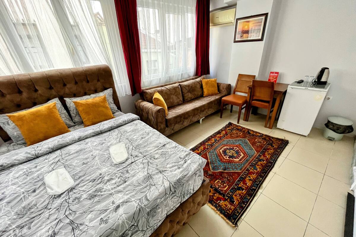 A hotel room with a bed, two sofas, a small desk, and a refrigerator.