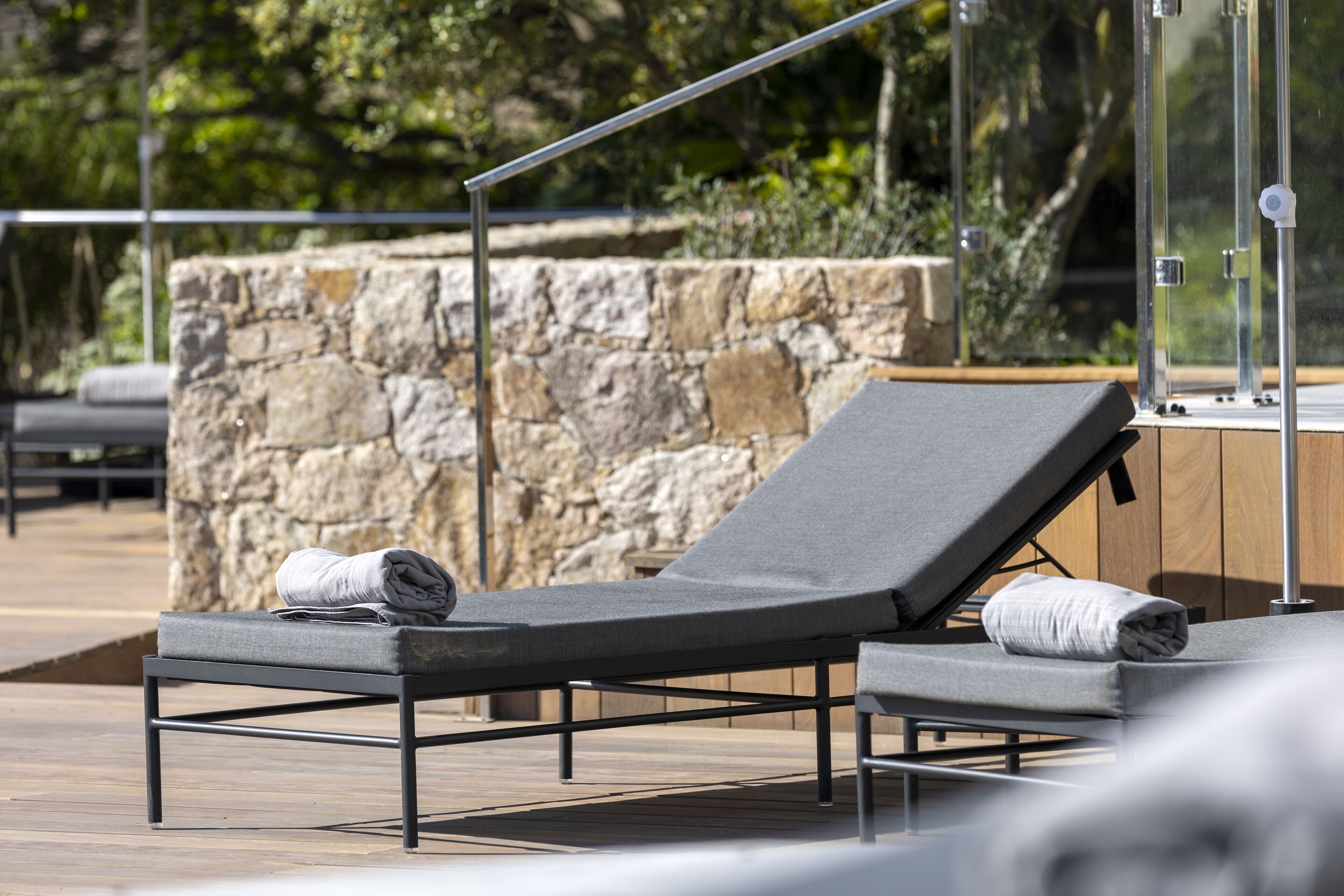 A lounge chair with a towel, a stone wall, and a wooden deck.