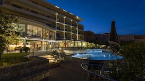 Un hôtel à plusieurs étages doté d’une piscine, d’un espace extérieur aménagé et d’une entrée bien éclairée.