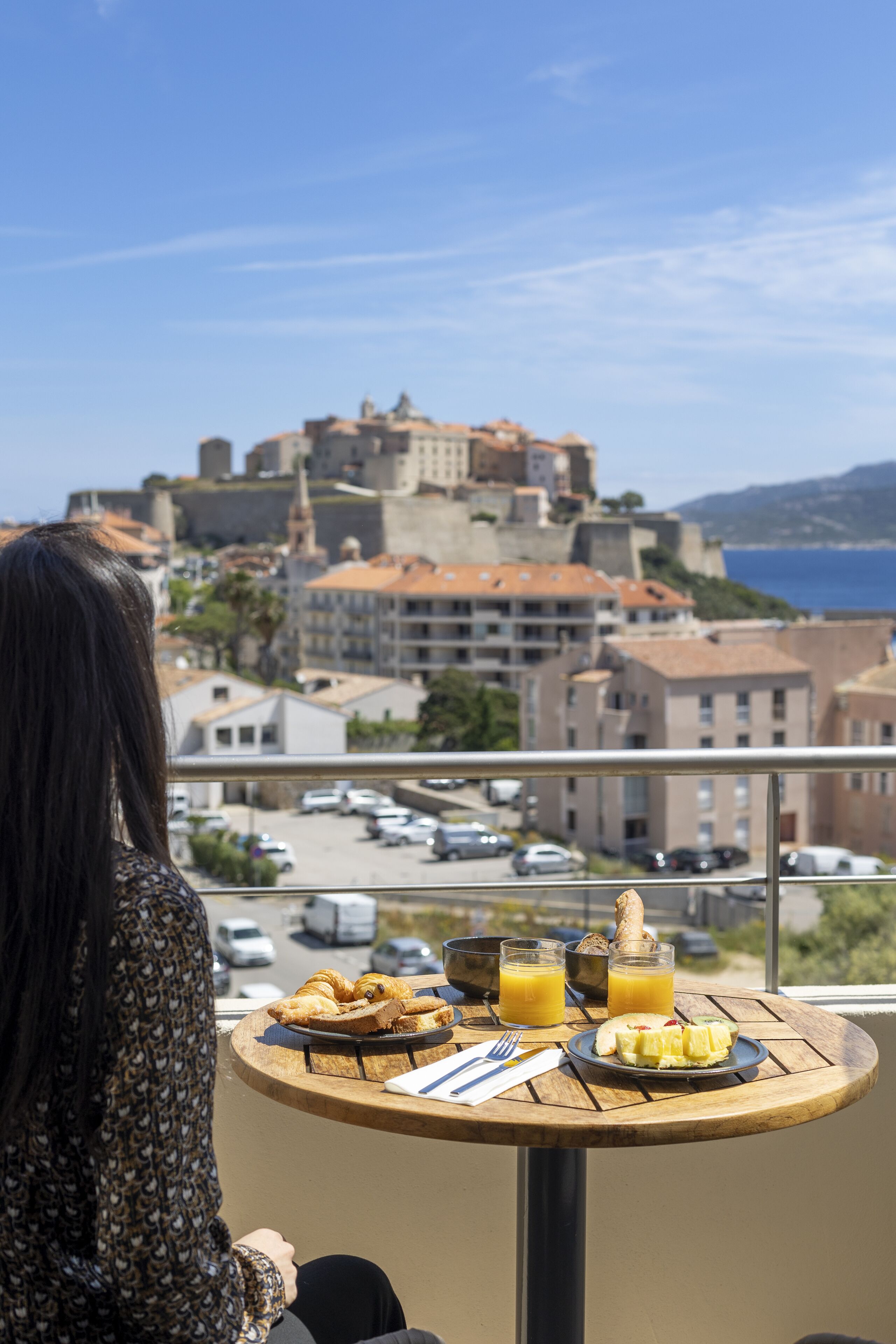 A balcony with a table set for breakfast, overlooking a historic town and the sea.
