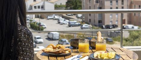 A balcony with a table set for breakfast, overlooking a historic town and the sea.