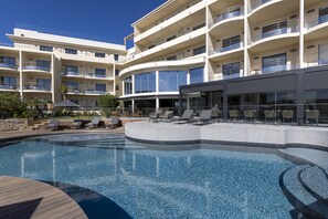 A modern hotel with a large pool, multiple balconies, and outdoor seating areas. - L'Acquale (Calvi)