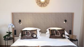 Ein ordentlich bezogenes Bett mit zwei Kissen, ein Nachttisch mit Lampe, eine Wandleuchte und ein kleiner Topfpflanze.