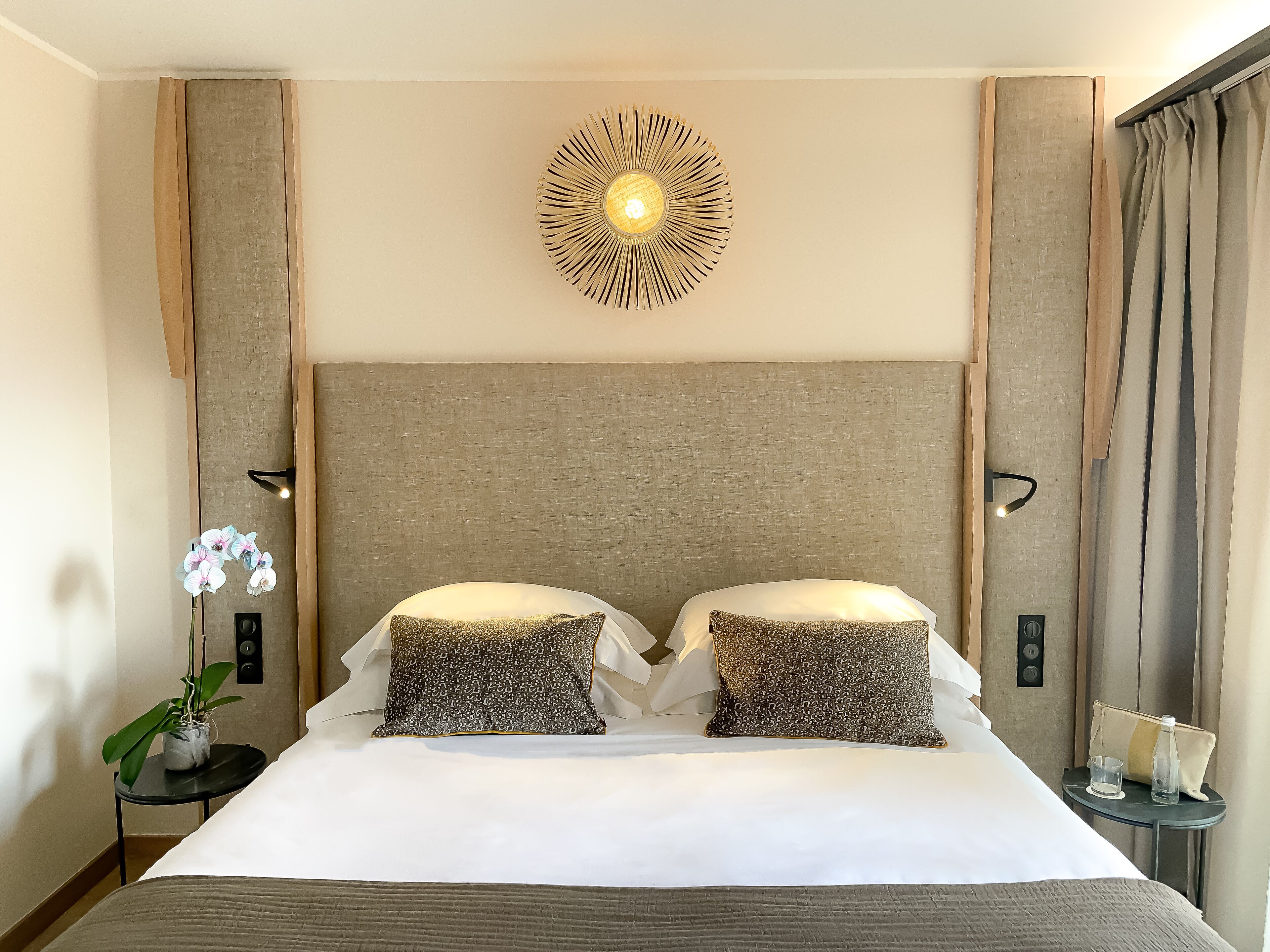 Ein Hotelzimmer mit einem großen Bett, zwei Kissen, einer Wandleuchte, einem kleinen Tisch mit einem Glas und einer Topfpflanze.