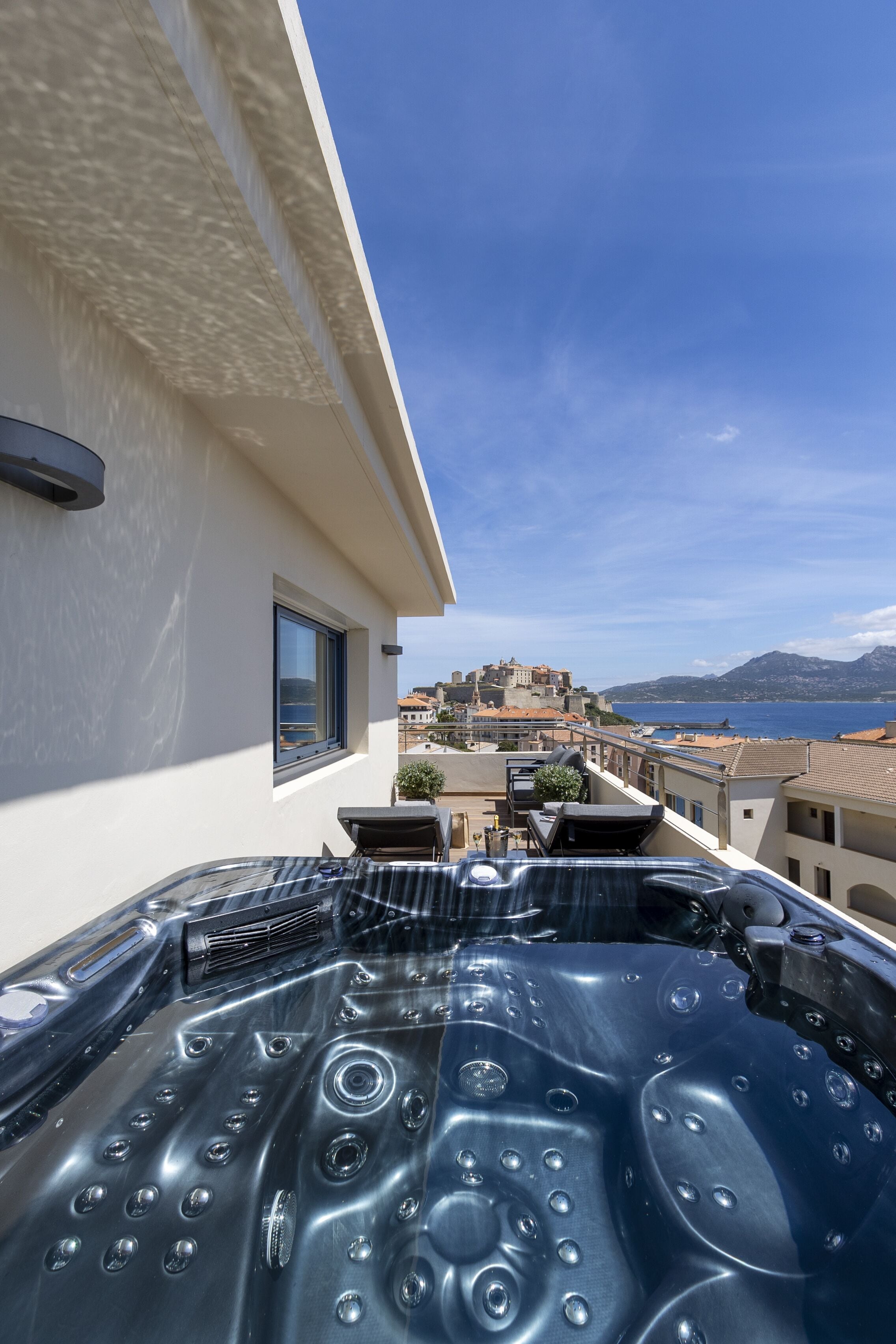 Ein modernes Gebäude mit Dachjacuzzi, großem Fenster und Blick auf eine historische Stadt sowie das Meer.