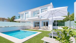 Een modern huis met twee verdiepingen, een zwembad, buitenzitplaatsen en een grote parasol.