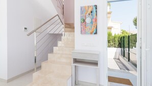 Een modern interieur met een beige trap, een witte console tafel en een kleurrijk abstract schilderij aan de muur.
