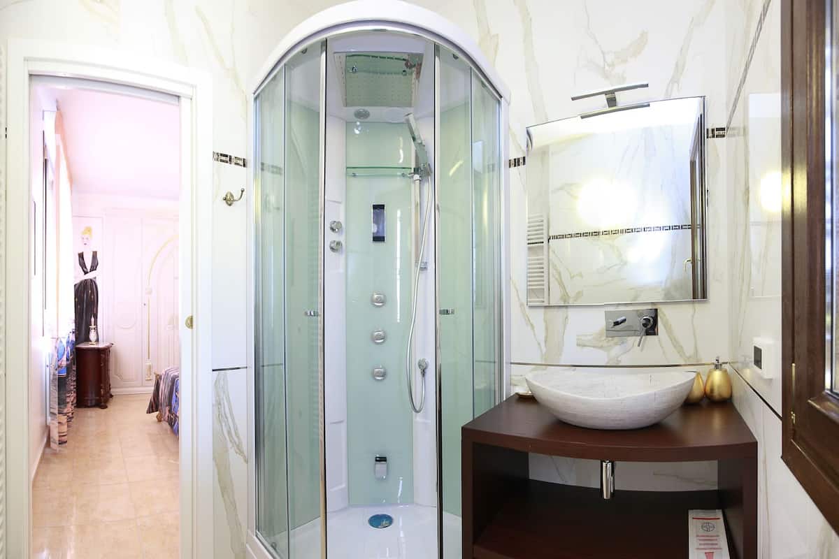 A modern bathroom with a glass-enclosed shower, a marble vanity, and a large mirror.