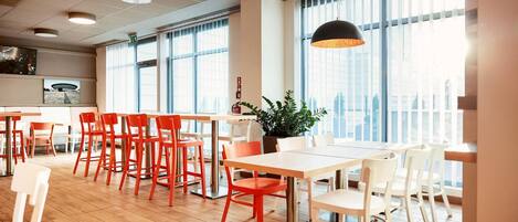Un comedor moderno con suelo de madera, sillas rojas y blancas, y grandes ventanales con vistas a la ciudad.