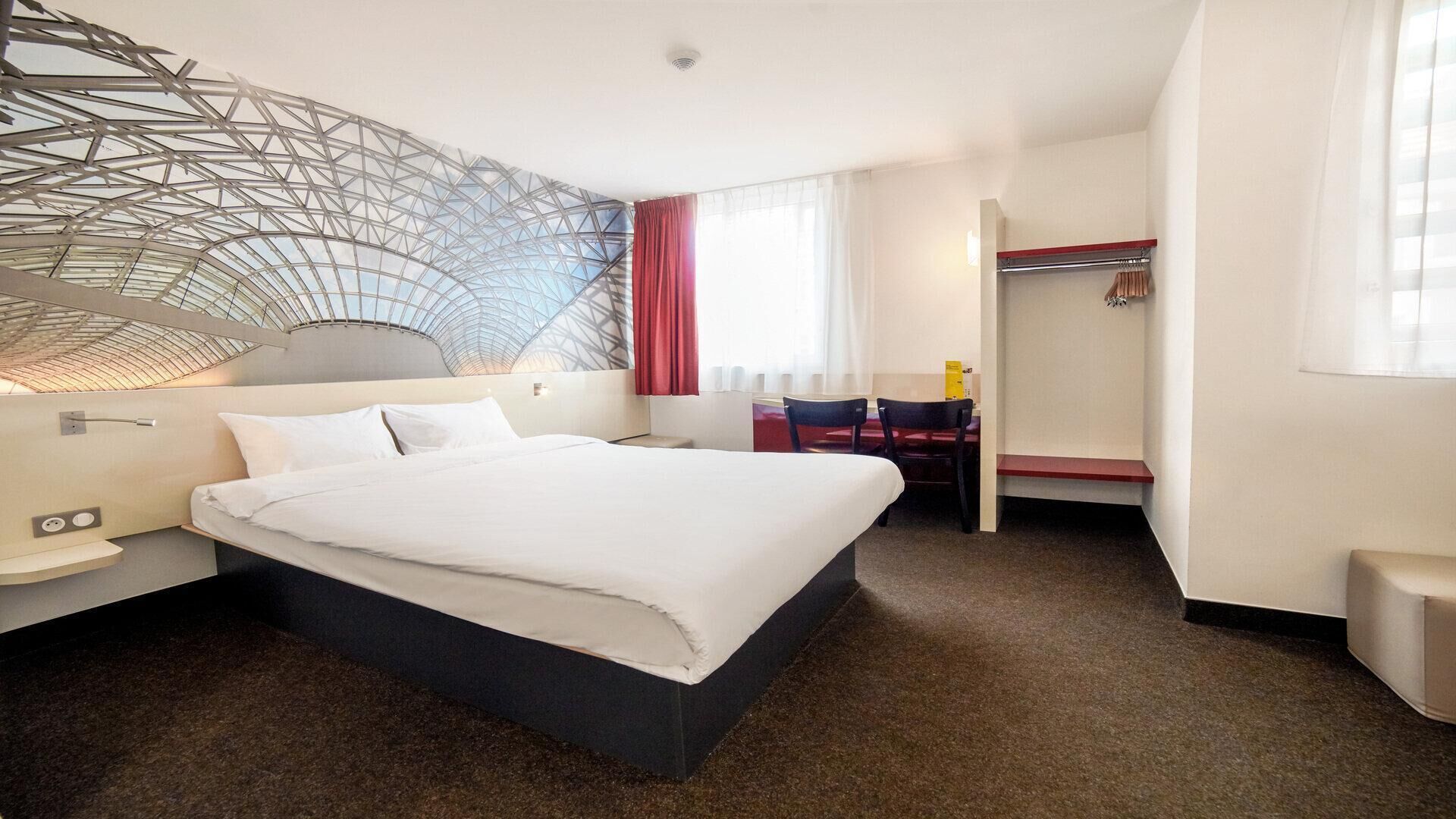 Moderni hotellihuone, jossa on suuri sänky, työpöytä ja erillinen vaatehuone.