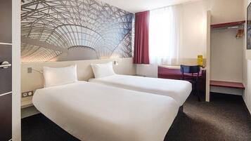Habitación de hotel con dos camas, un escritorio, una silla, un perchero y una pared con diseño geométrico.