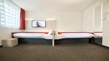 Una habitación de hotel con dos camas, un televisor montado en la pared, una mesita de noche y una cortina roja.