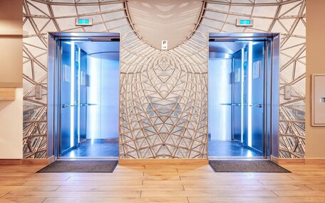 Two elevator doors with a geometric patterned wall behind them.