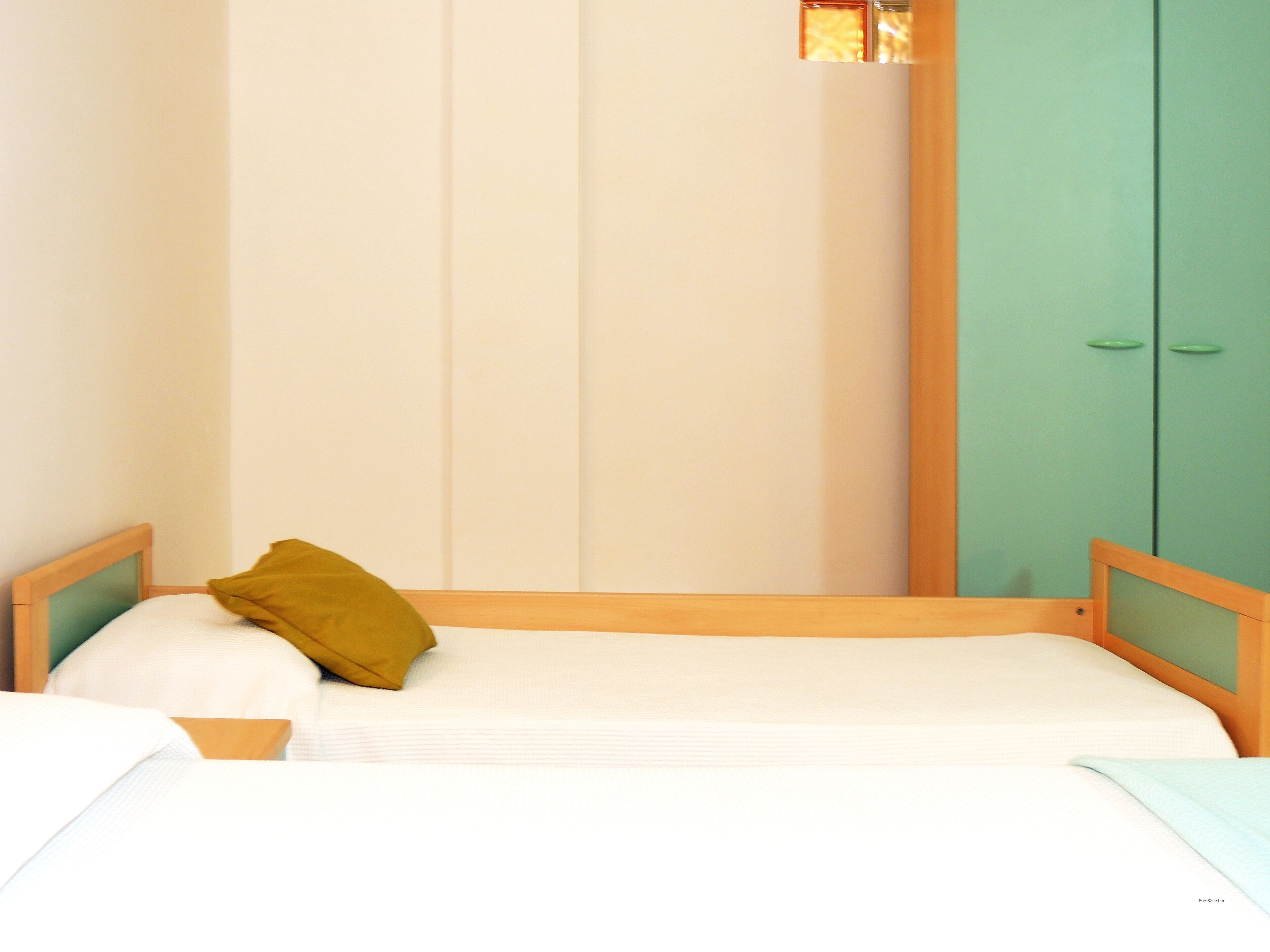 Una habitación pequeña con una cama individual, cabecera de madera, armario verde y pared de tono claro.