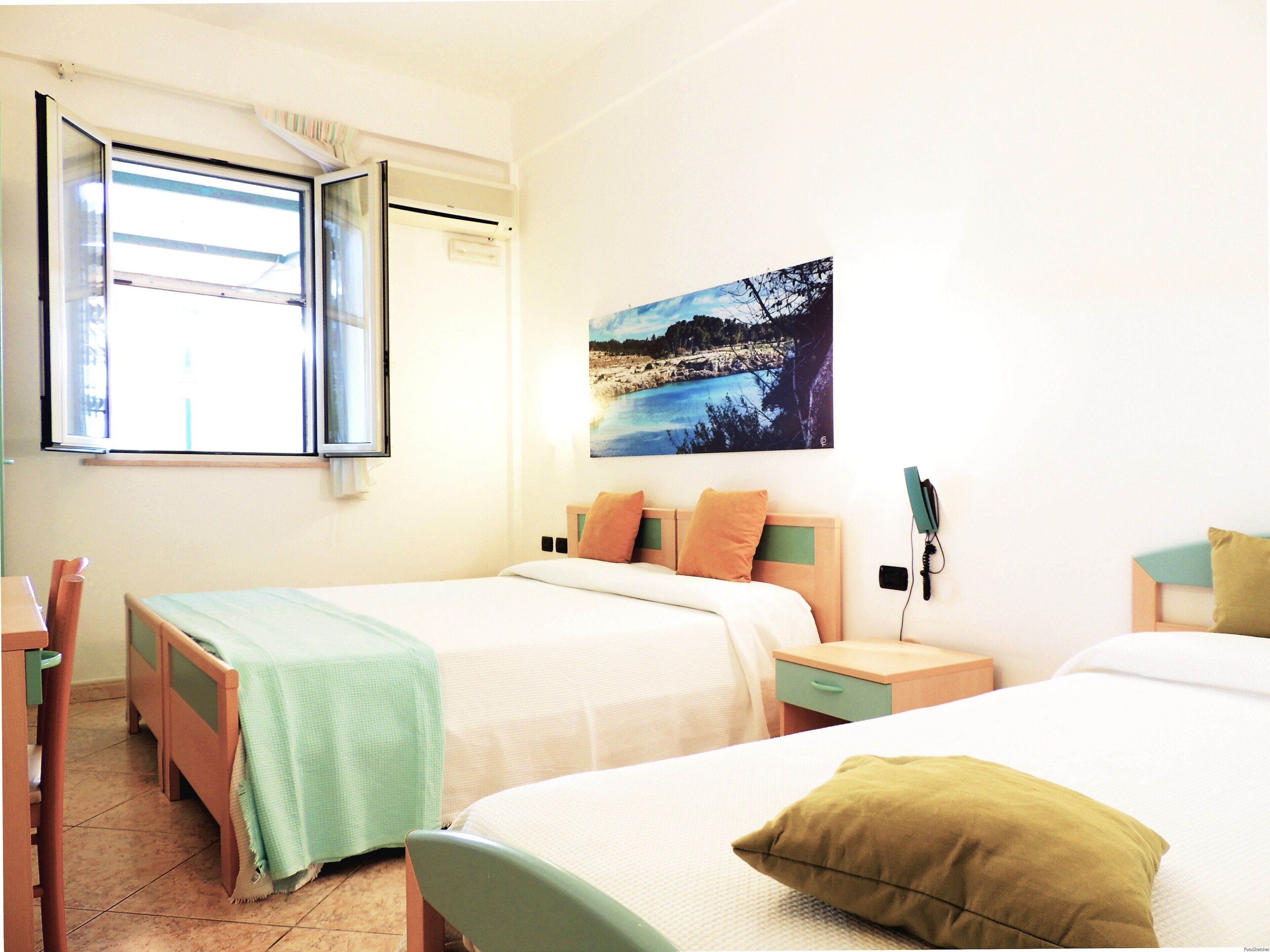 A hotel room with two beds, a window, a painting, and a bedside table with a phone.