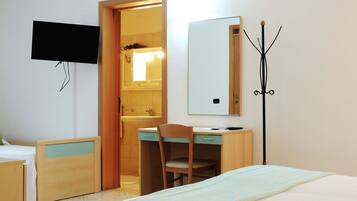 A bedroom with a bed, a desk with a chair, a TV mounted on the wall, and a coat rack.