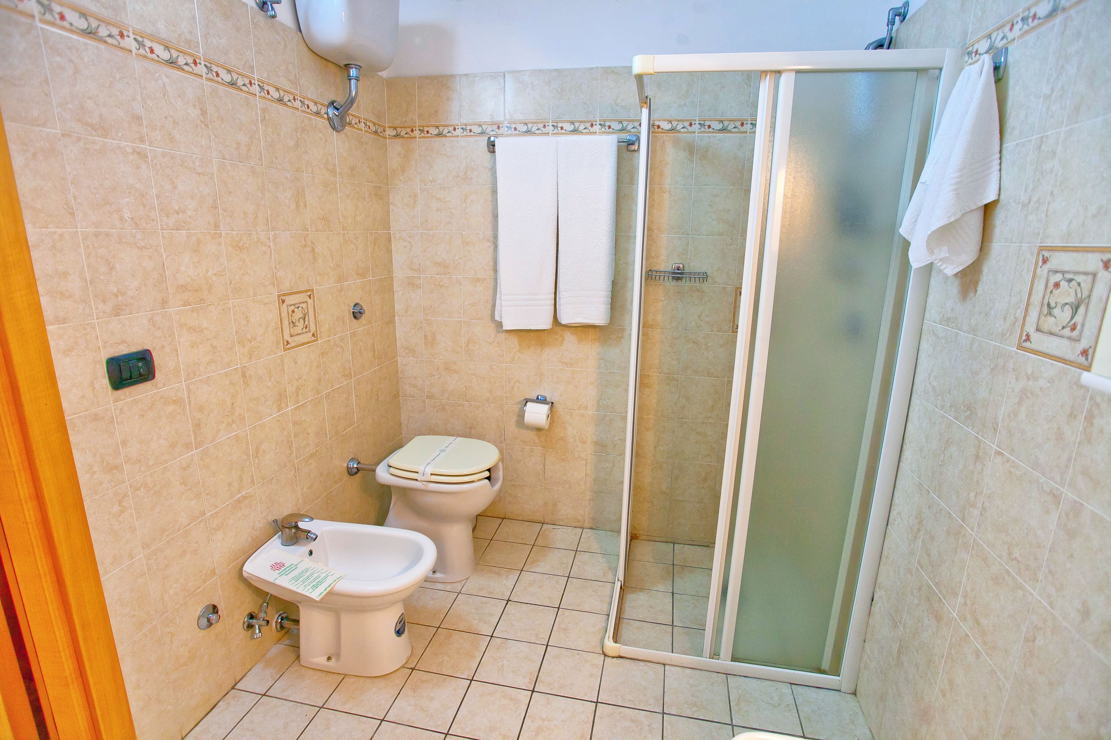 Une salle de bain avec deux toilettes, un bidet, une douche à parois de verre et un lavabo.