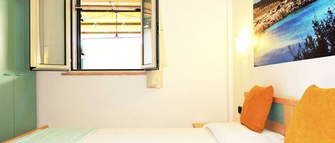 A bedroom with a bed, a window, a wall-mounted air conditioner, and a painting of a landscape.