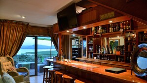 Um bar com vista para o oceano, móveis de vime e diversos tipos de garrafas.