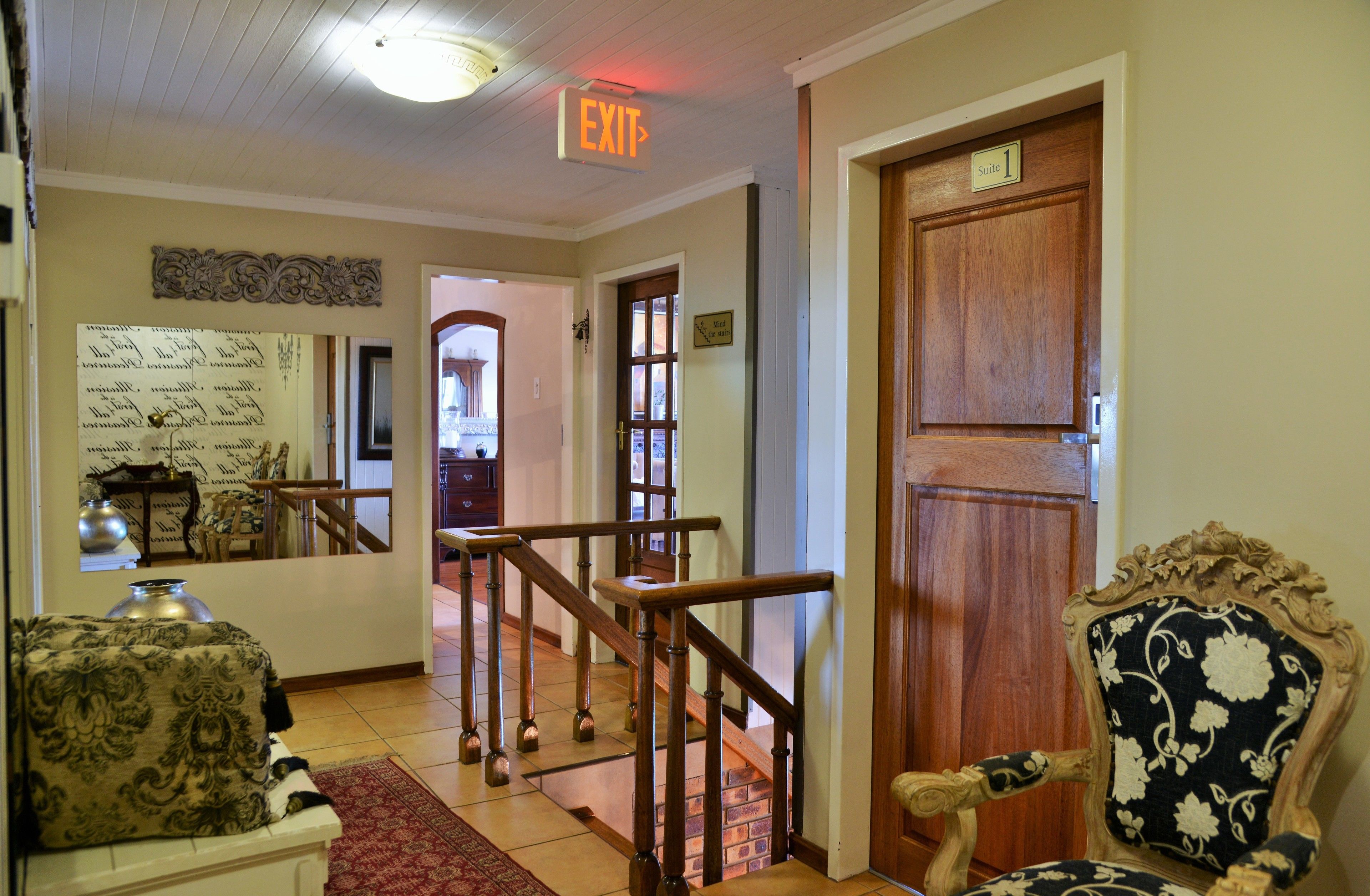 A hotel lobby with a wooden staircase, a sitting area with a patterned sofa, and a door labeled "Suite 1".