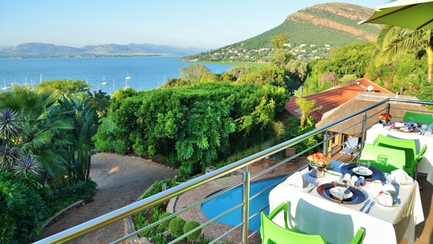Varanda com piscina, área de refeições e vista para o mar e montanhas.