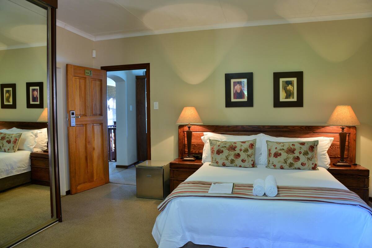 A hotel room with a large bed, two bedside tables, a nightstand, a mirror, and a door leading to another room.