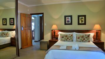 Una habitación de hotel con una cama grande, dos mesitas de noche, un tocador, un espejo y una puerta que da a otra habitación.