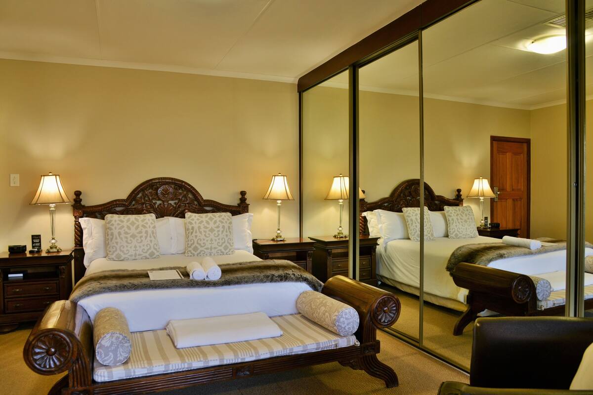 A hotel room with a large bed, two bedside tables with lamps, a mirror, and a chair.