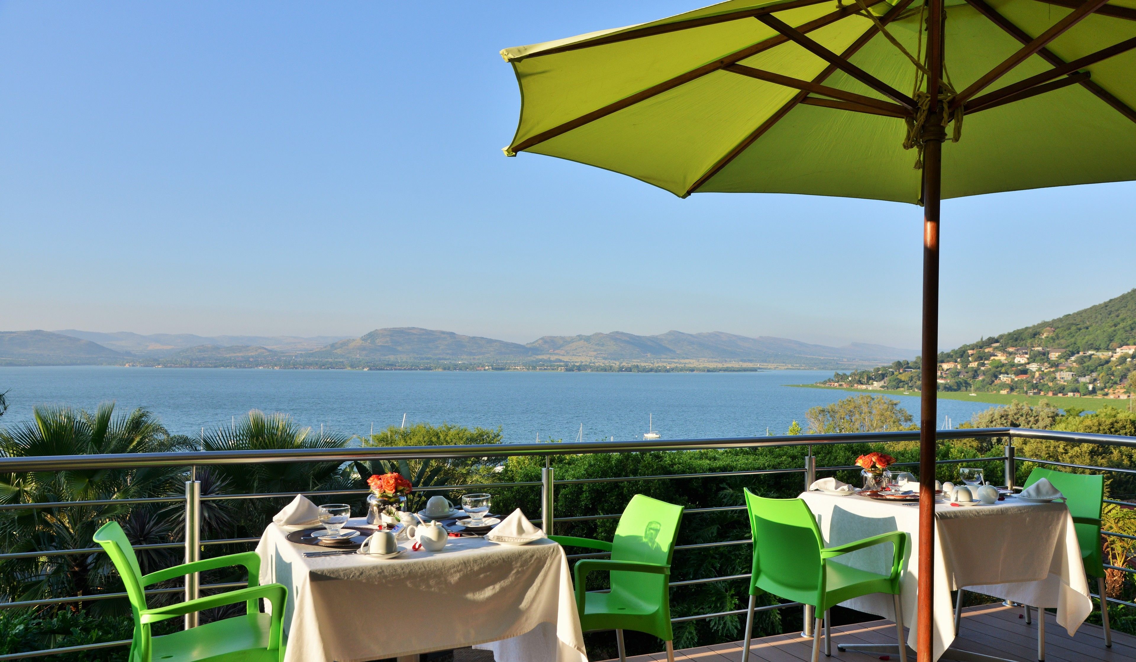 An outdoor dining area with a table set for two, overlooking a body of water and distant hills.