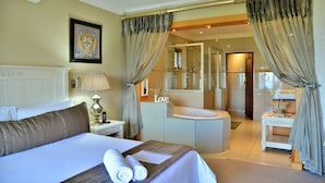 Quarto de hotel com cama, mesa de cabeceira com abajur, banheiro com banheira e espelho.