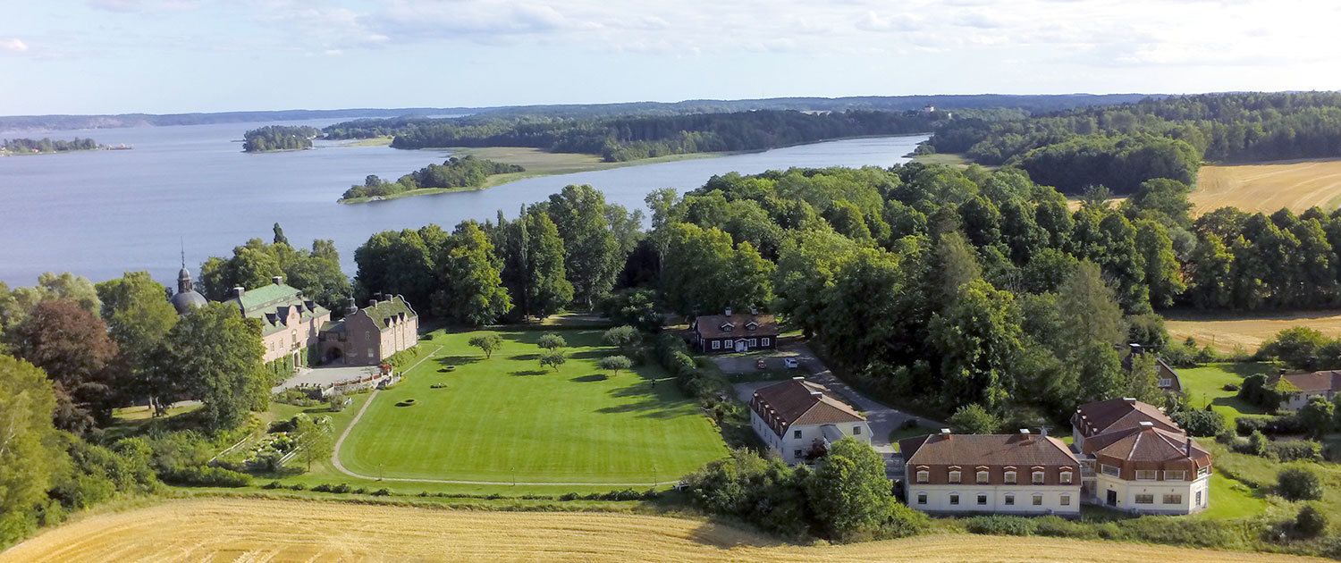 A large estate with a well-maintained lawn, several buildings, and a body of water in the background.