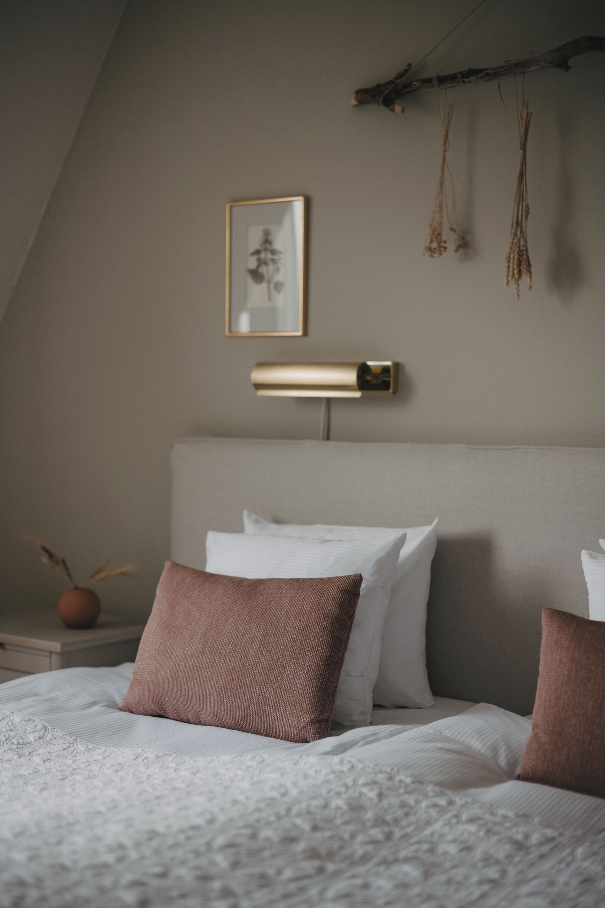 A neatly made bed with white and brown bedding, a wall-mounted lamp, and a framed picture above it.