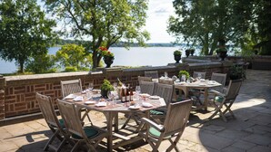 An outdoor dining area with brick walls, wooden tables, and chairs, overlooking a body of water. - Engsholms Slott - Adults Only (Morko)