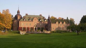 A large, historic building with a prominent tower and a green roof, surrounded by a well-maintained lawn.