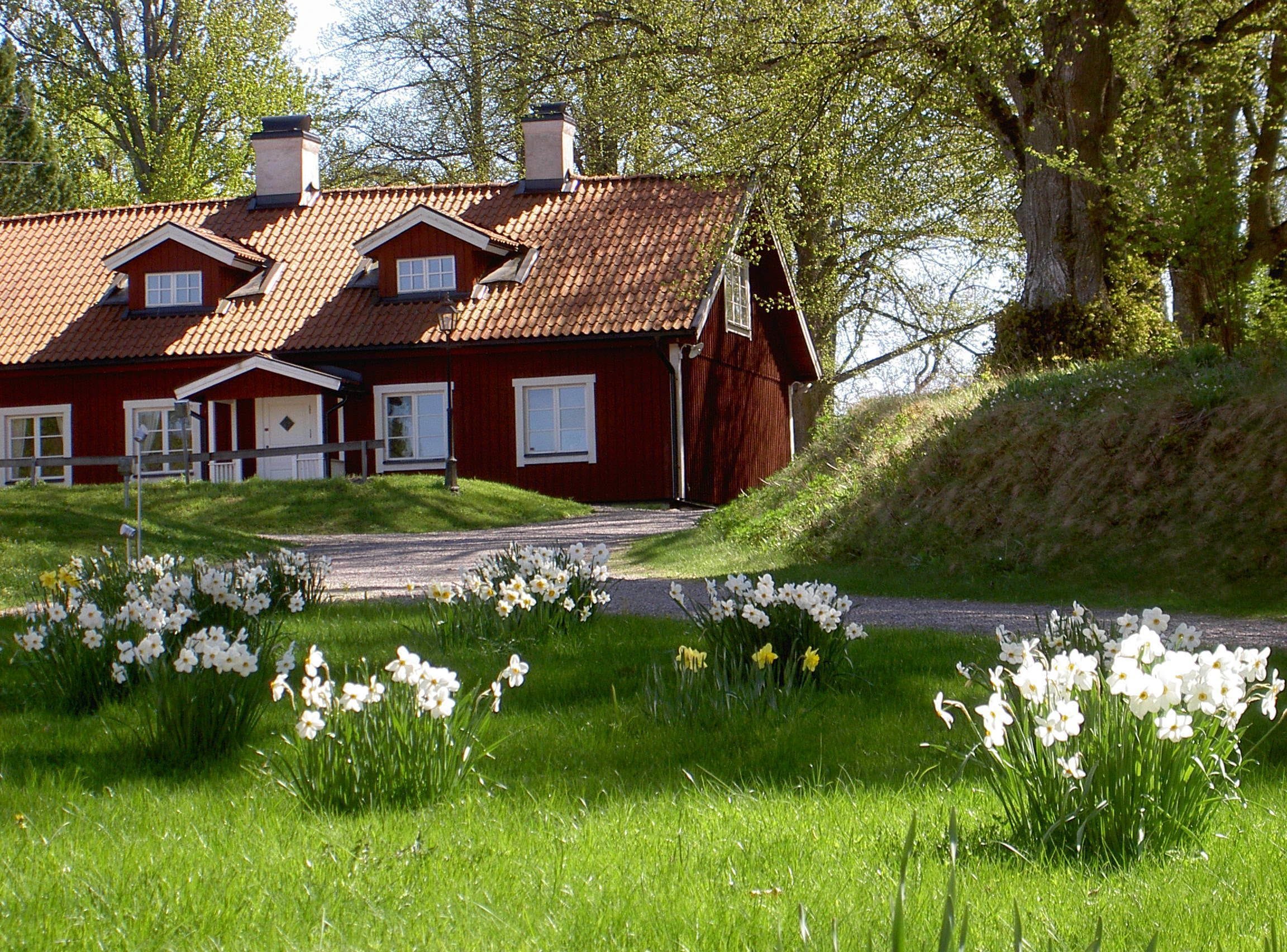 A red wooden house with a tiled roof, a front porch, and a driveway leading to the entrance.