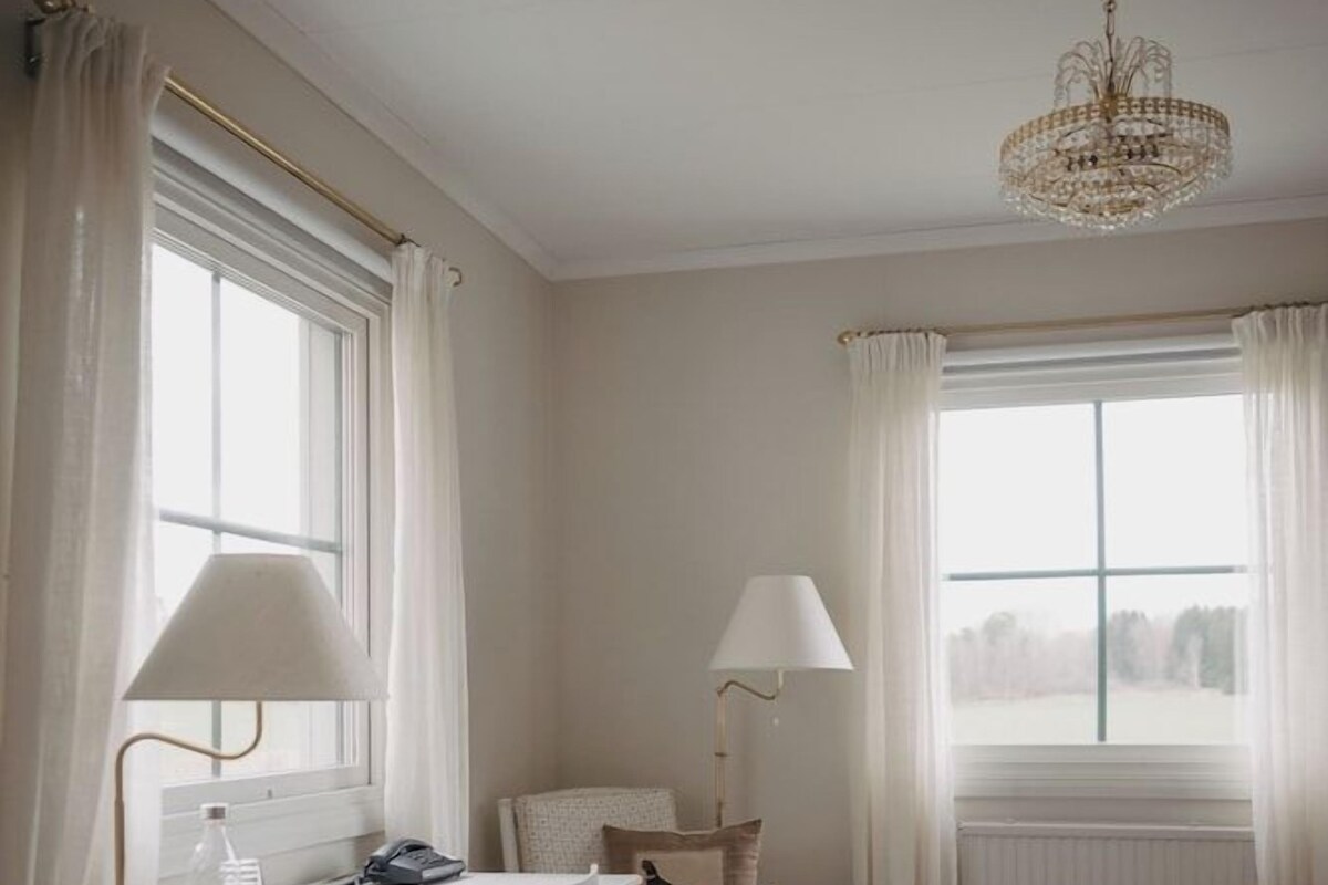 A hotel room with a bed, a desk with a lamp, a chair, and a window with curtains.