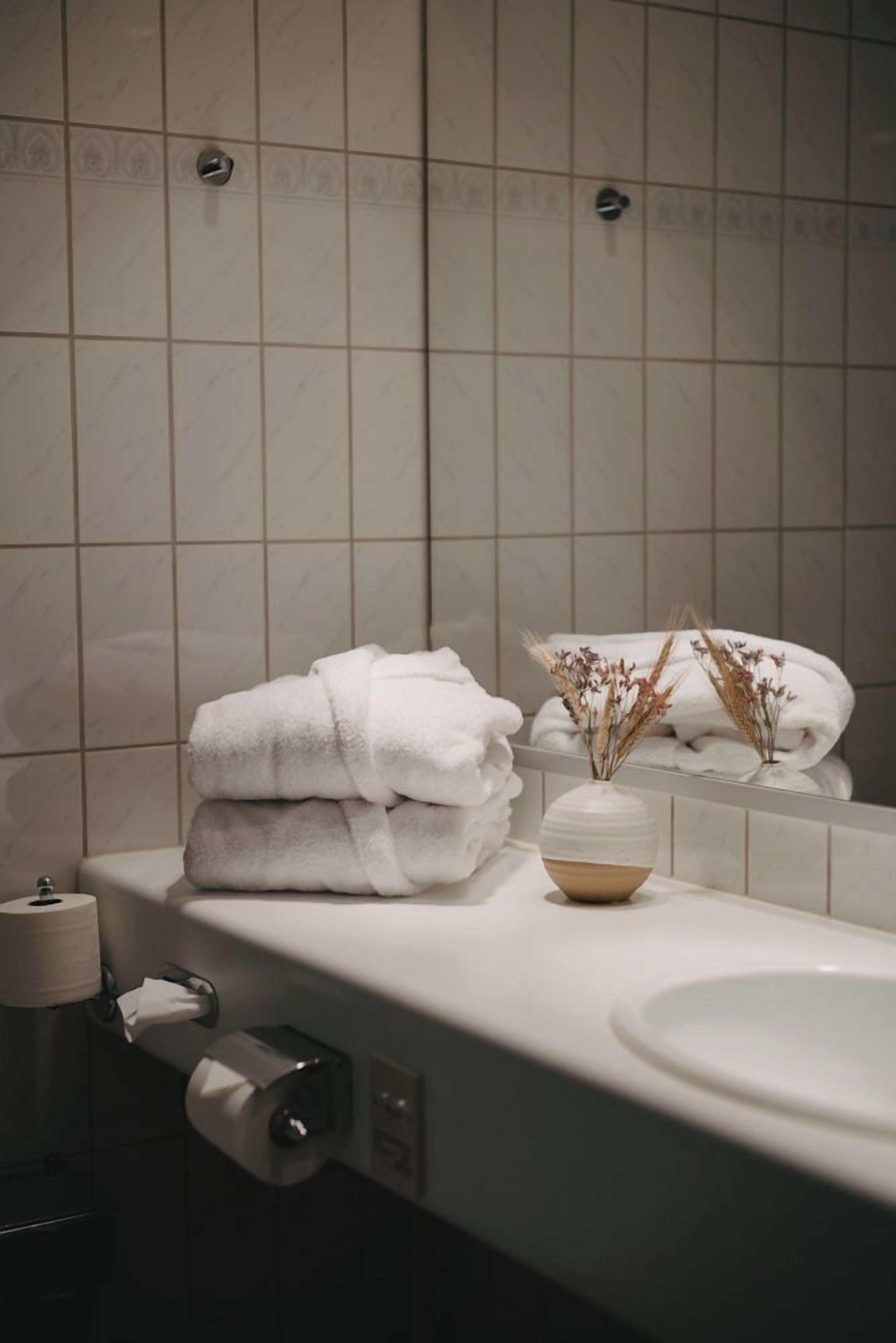 Un baño con lavamanos, papel higiénico y un florero con flores secas.
