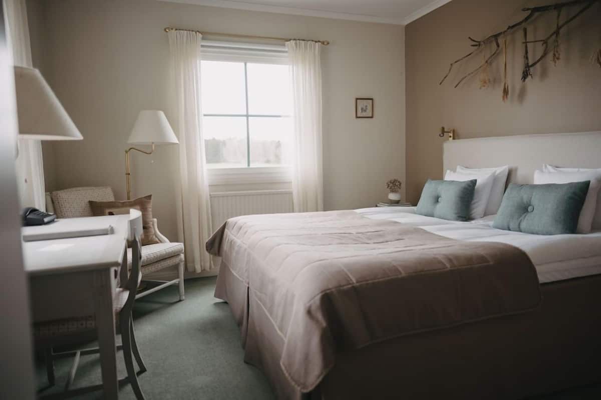 A hotel room with a bed, a desk, a chair, a lamp, and a window with curtains.