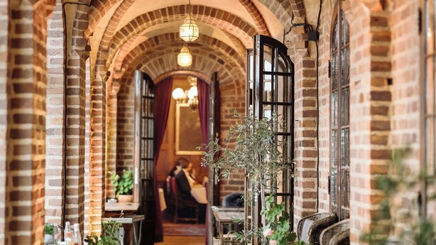 A corridor with brick arches, hanging lights, and a plant. - Engsholms Slott - Adults Only (Morko)