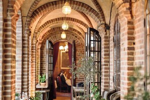 A corridor with brick arches, hanging lights, and a plant. - Engsholms Slott - Adults Only (Morko)