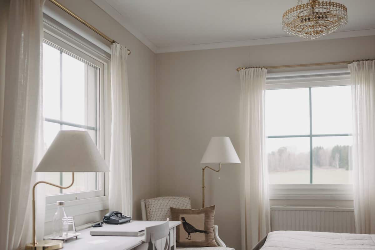 A hotel room with a bed, a desk with a lamp, a chair, and a window with curtains.