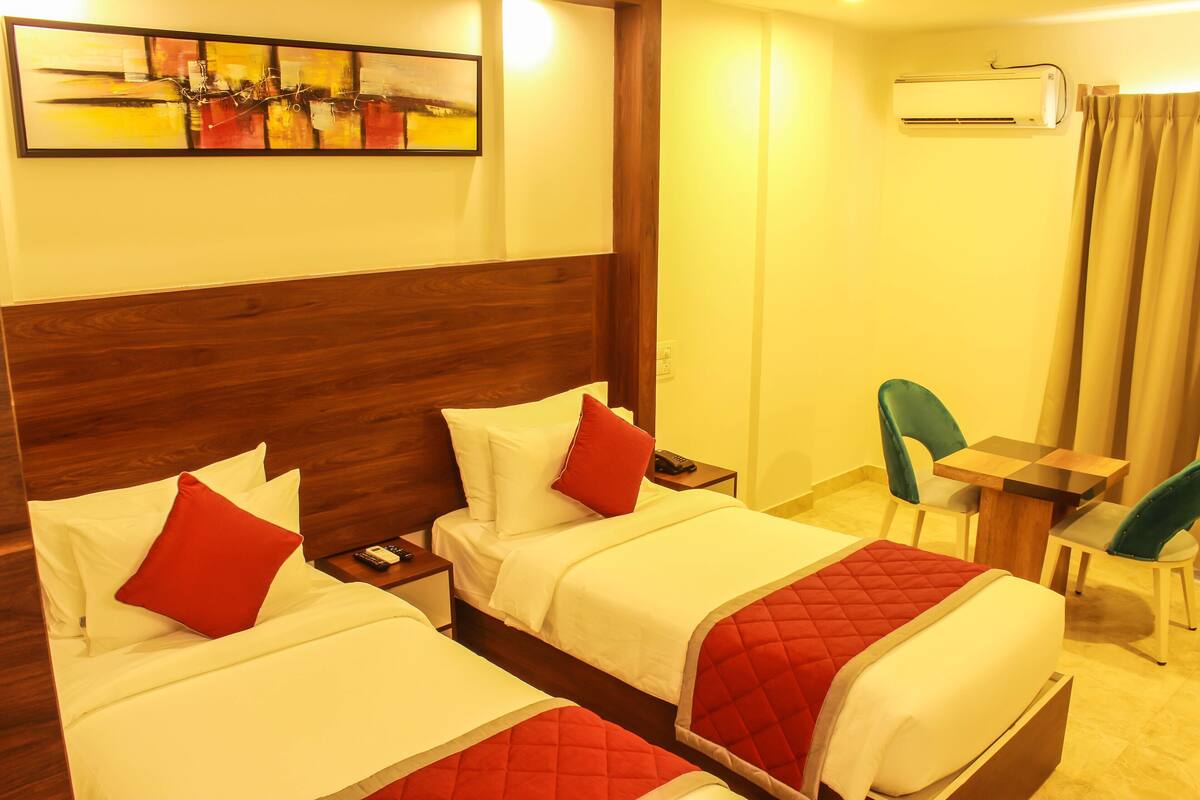 A hotel room with two beds, a desk, a chair, an air conditioner, and a painting on the wall.
