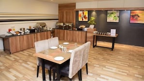 A dining area with a wooden table set for four, a buffet counter with various food items, and a small side table with a plant. - Rest Inn By Sublime (Bengaluru)